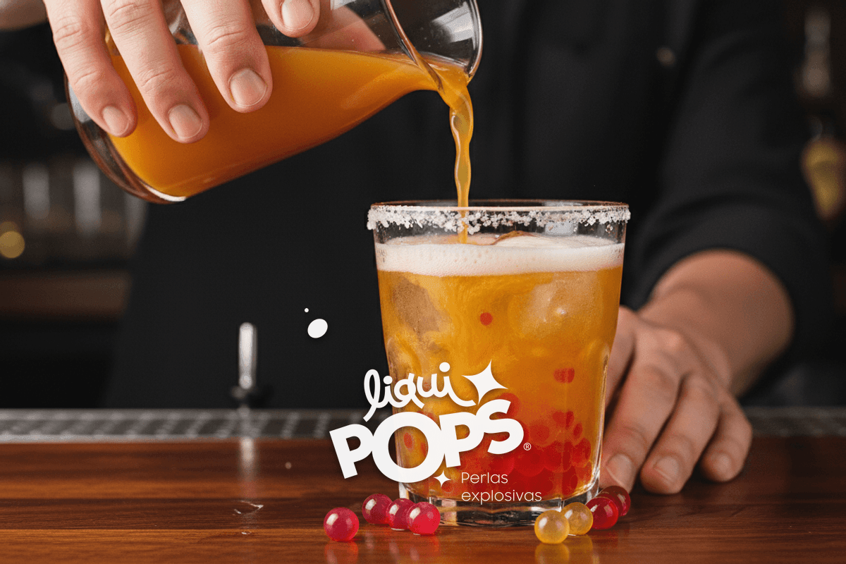 Action shot of a bartender pouring 1 oz of bright orange maracuyá syrup into a salt-rimmed glass with ice and beer.