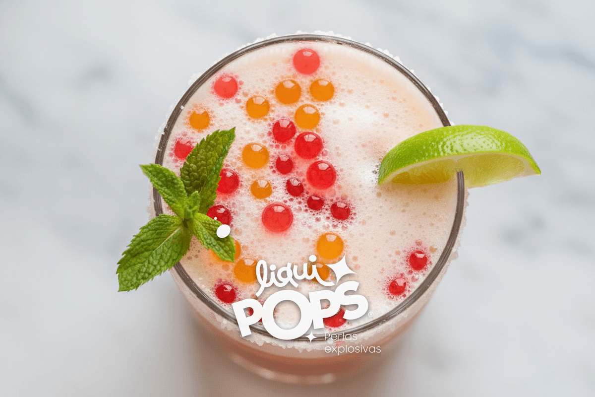 Top-down of finished michelada with red and yellow popping boba pearls floating on the foam, mint sprig and lime wedge g.
