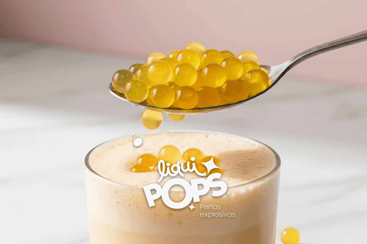 Side-view of yellow Maracuyá popping boba pearls being scooped with a stainless steel spoon onto michelada foam.