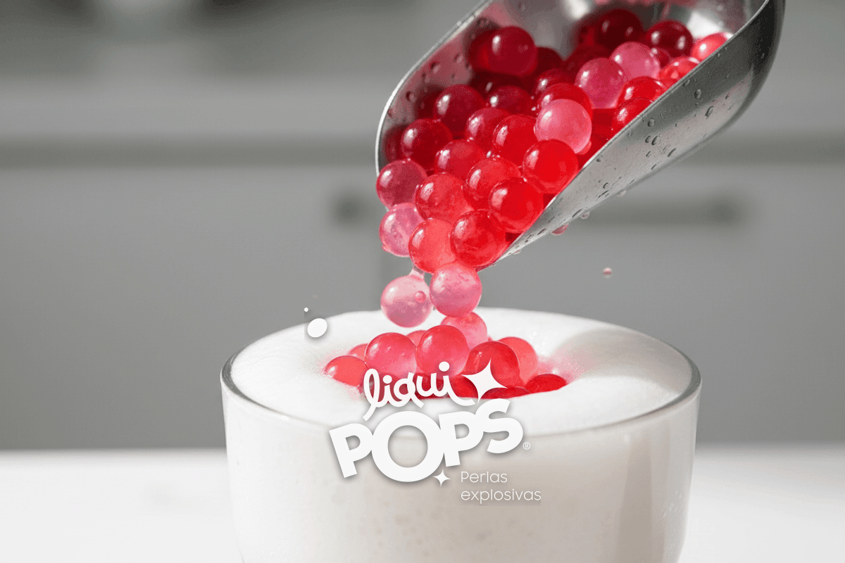 Macro of pink and red popping boba pearls being added with a metal scoop on top of the soda foam.