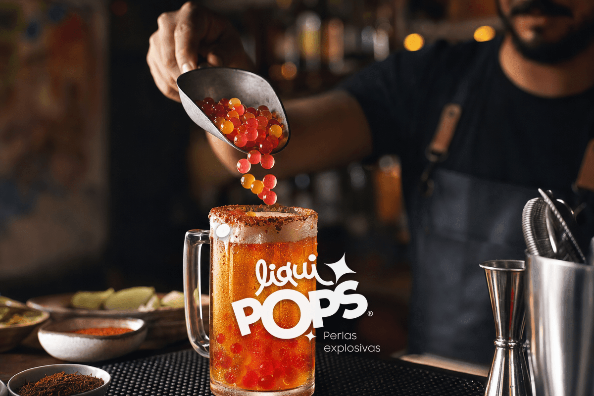 Action shot of a bartender hand pouring multicolor popping boba pearls into a tall michelada glass from a stainless stee.