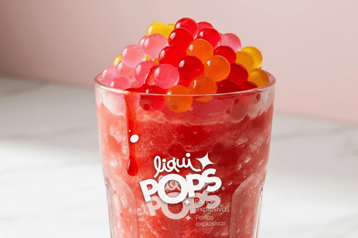 Close-up of a single tall glass of red strawberry granizado with mound of popping boba pea — perlas explosivas granizados LiquiPops Colombia