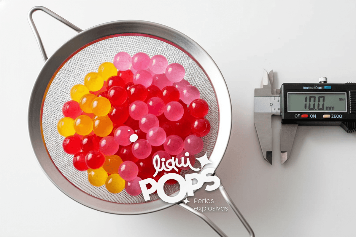 Top-down close-up of a stainless steel sieve filled with calibrated round popping boba pearls being measured, a digital .